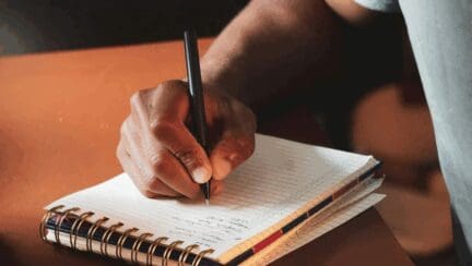 Anonymous man writing a to-do list in a white ruled paper notebook.
